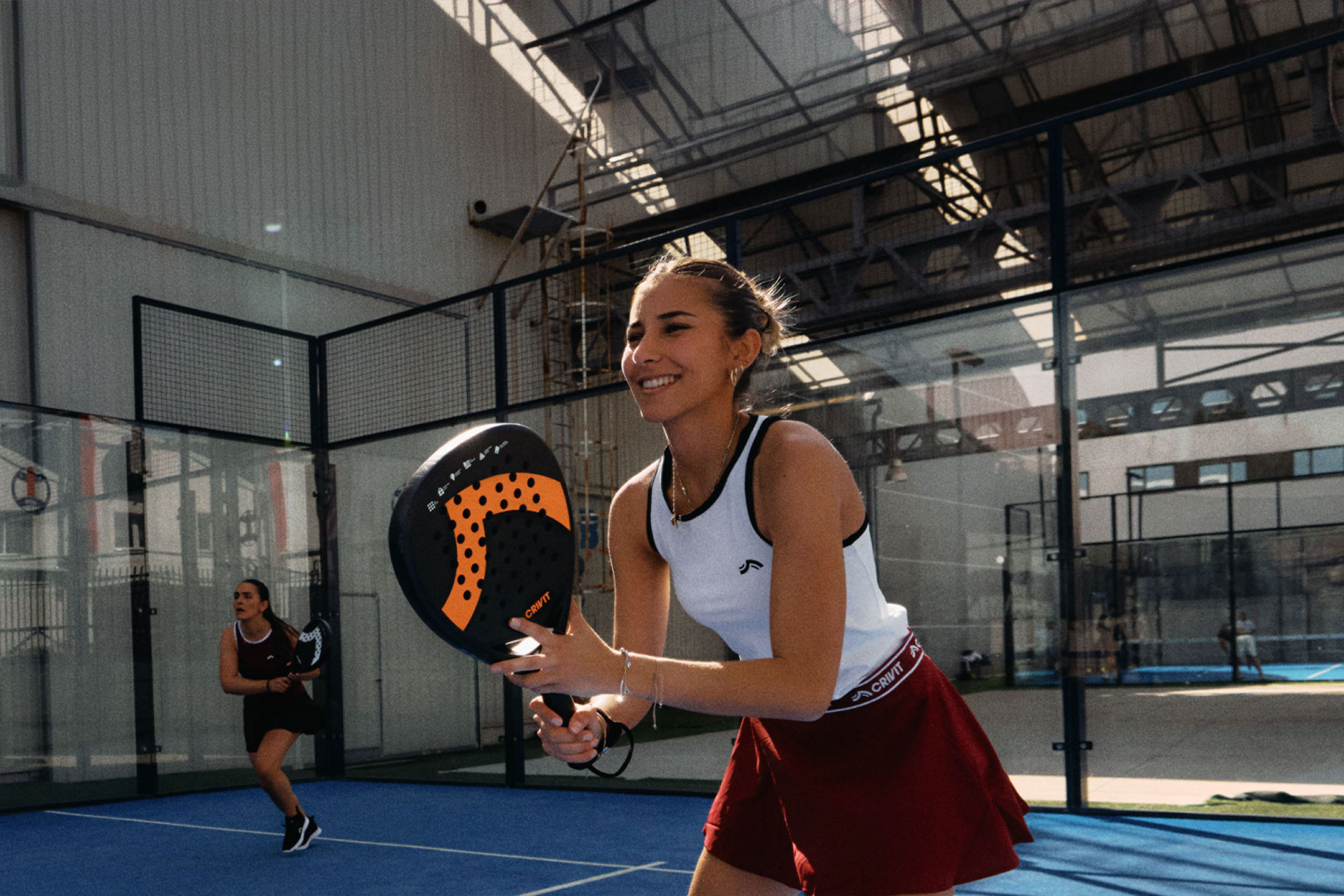 Obrázok bol vygenerovaný pomocou AI: Dve ženy hrajú padel tenis, jedna sa usmieva a drží raketu, na modrom kurte.
