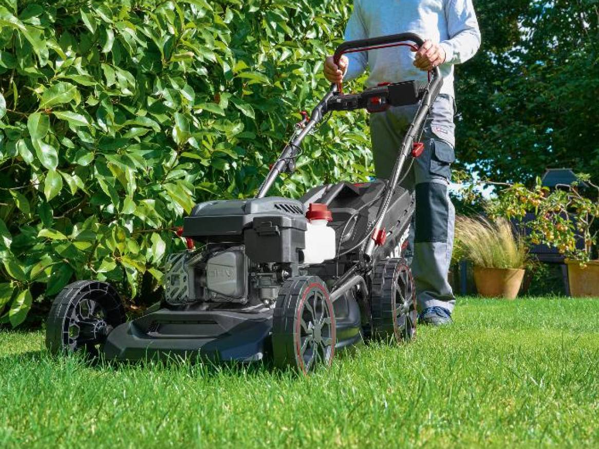 Muž kosí trávnik s benzínovou kosačkou na trávu.