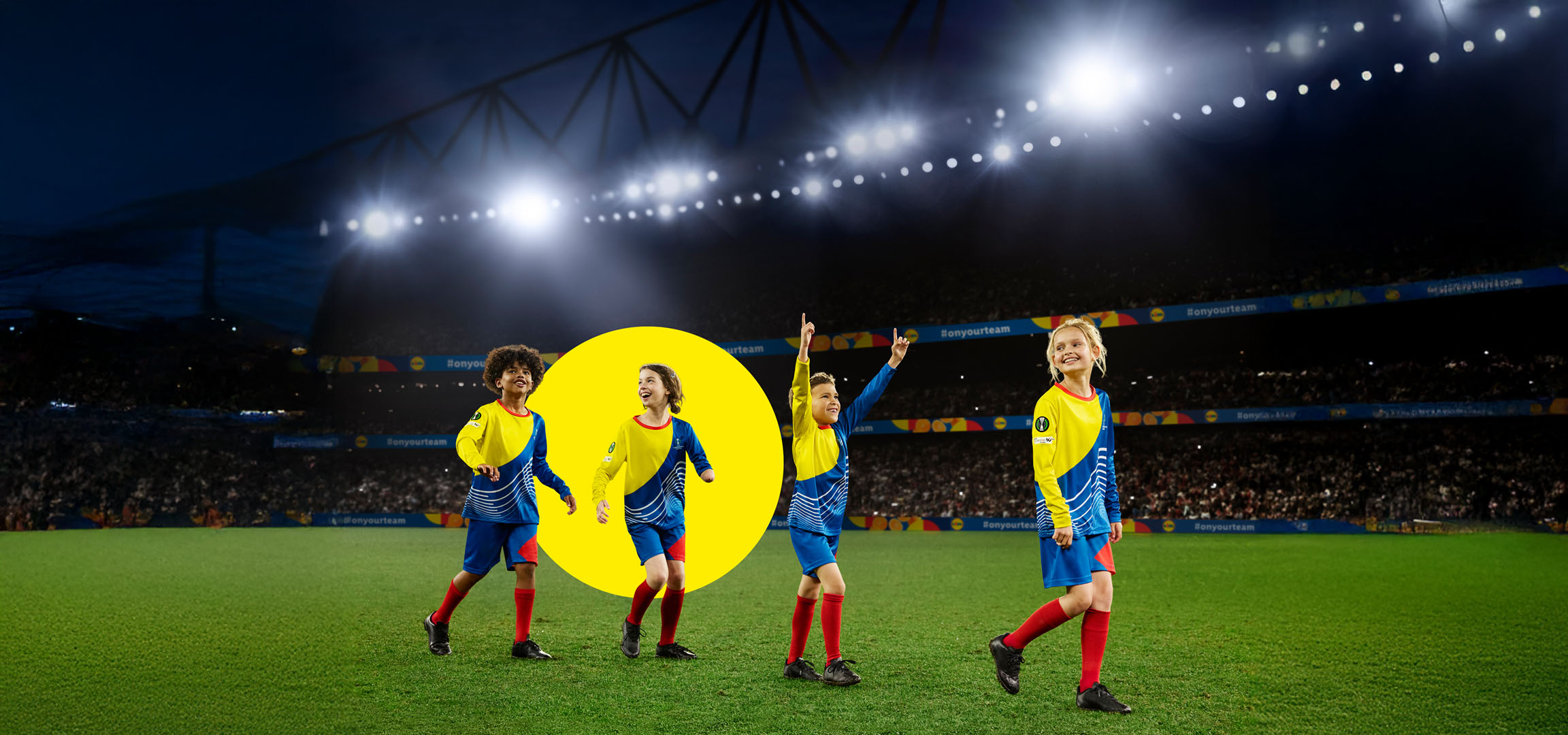 Deti vo futbalových dresoch na ihrisku pod svetlami štadióna.