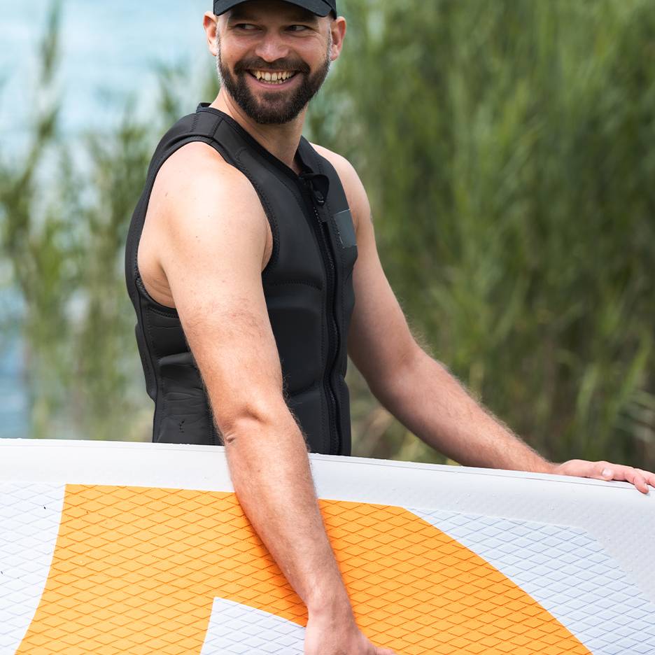 Usmievajúci sa muž v čiernej záchrannej veste drží paddleboard.