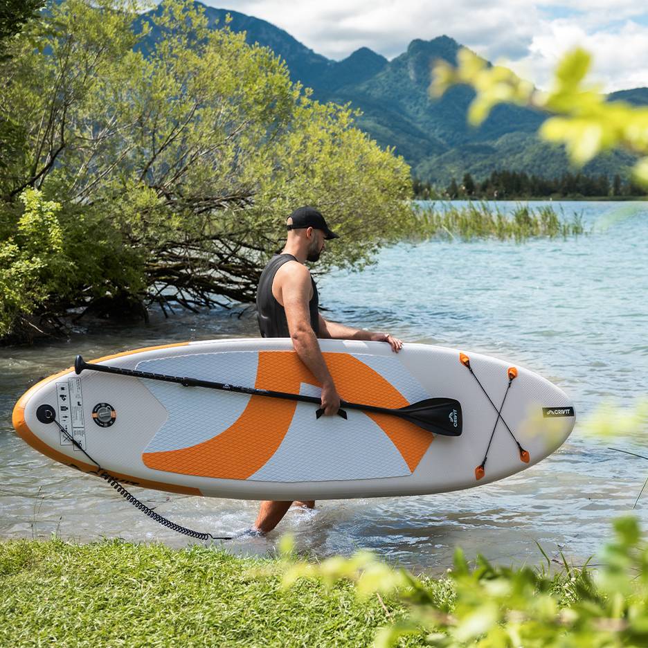 Muž s paddleboardom CRIVIT vo vode, pripravený pádlovať.