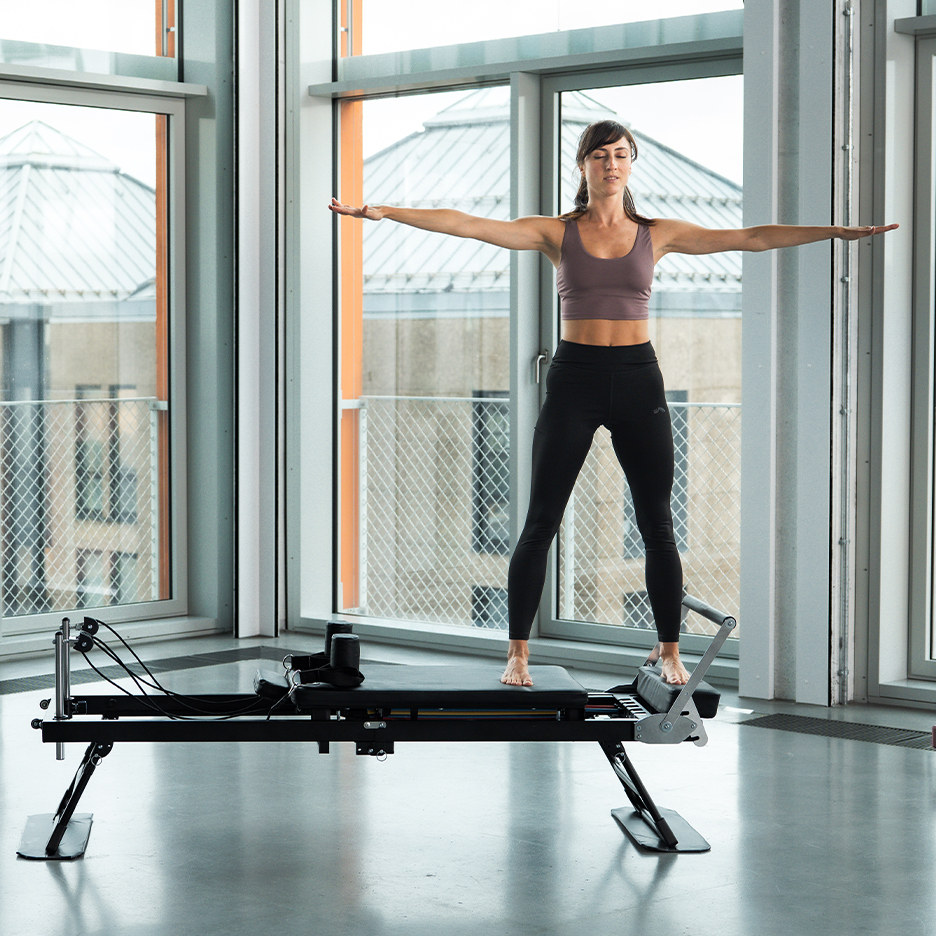 Žena cvičiaca Pilates na reformeri s rozpaženými rukami.