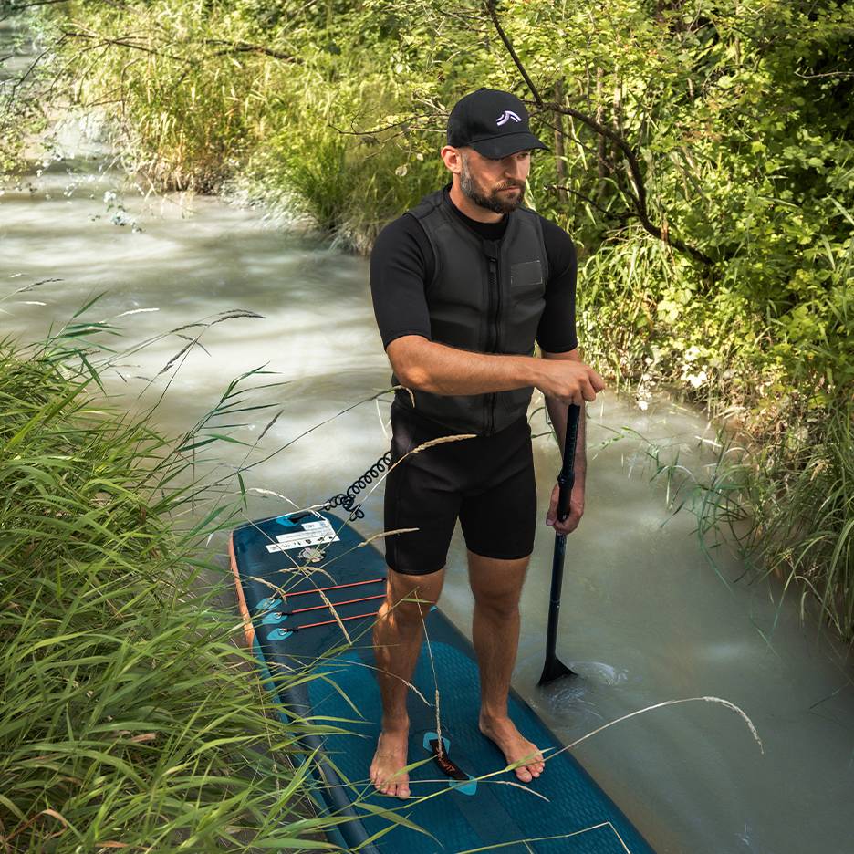 Muž na paddleboarde v rieke, v neopréne a záchrannej veste.