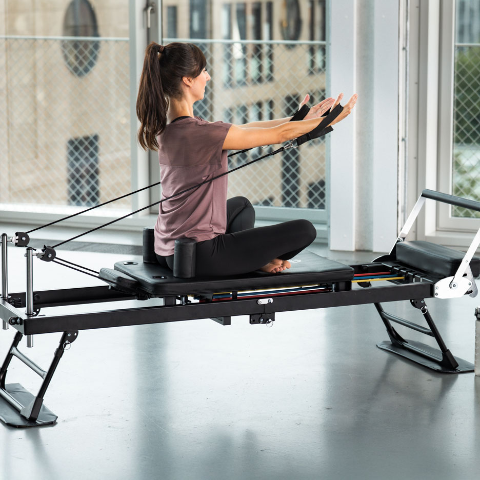 Žena cvičiaca na pilates stroji s odporovými pásmi.