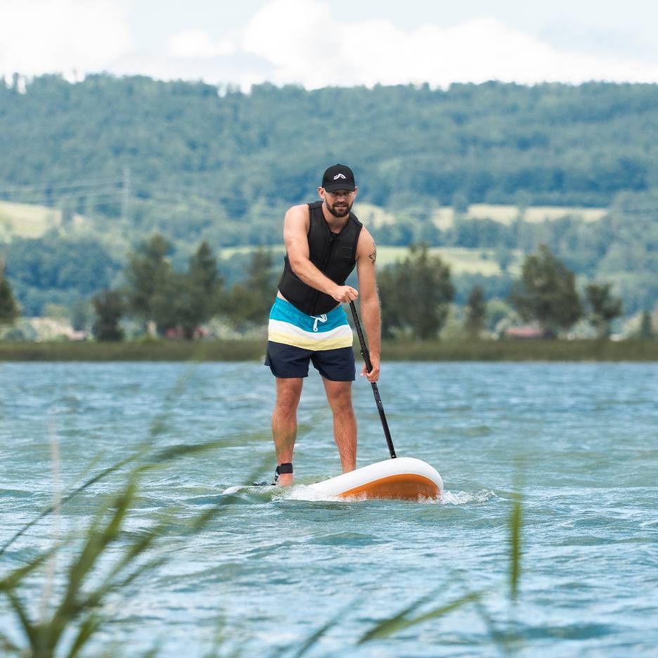Muž na paddleboarde na jazere, v záchrannej veste a plavkách.