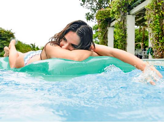 Žena relaxuje na zelenom plávajúcom kruhu v bazéne.