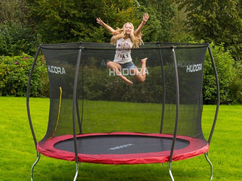 Dievča skáče na červenej trampolíne Hudora s ochrannou sieťou.