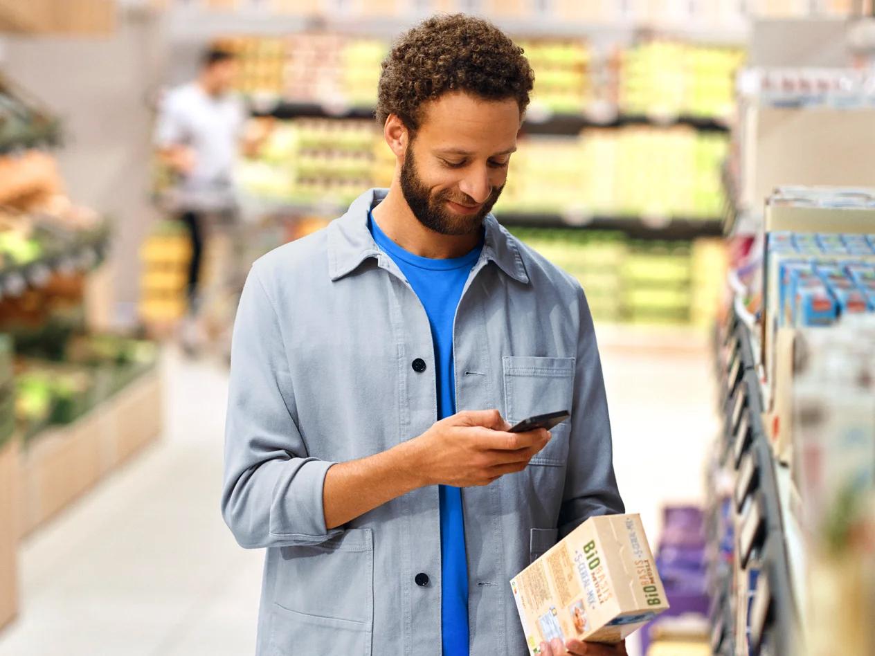 Muž v supermarkete skenuje krabicu s cereáliami pomocou smartfónu.