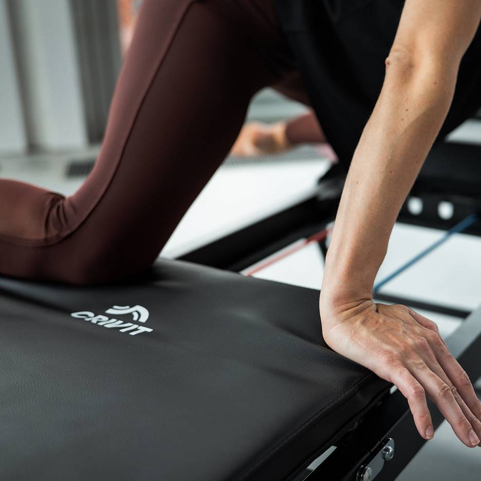 Žena cvičiaca na fitness stroji Crivit v hnedých jogových nohaviciach.