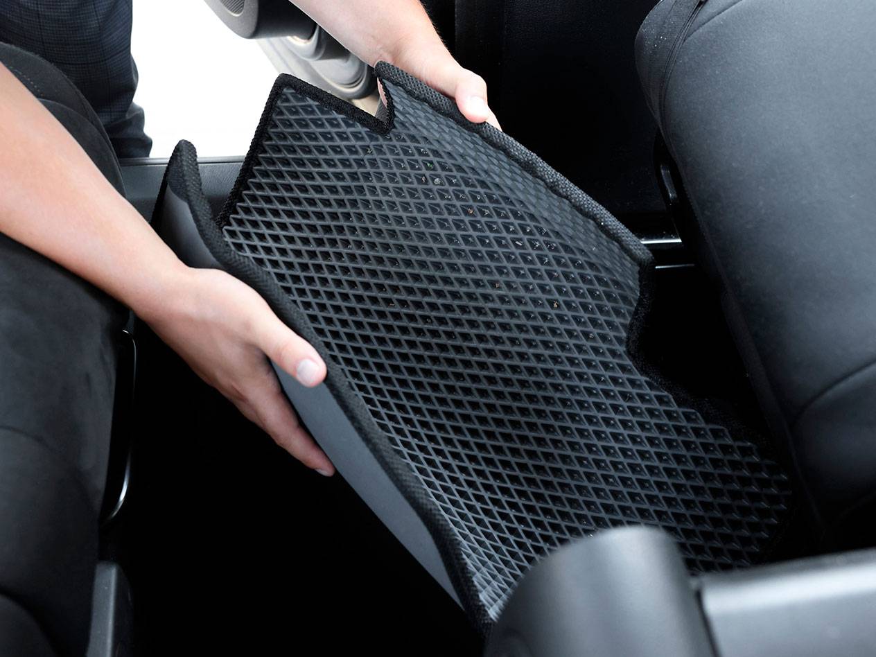 Osoba vkladá čiernu gumovú autokoberček s diamantovým vzorom do vozidla.