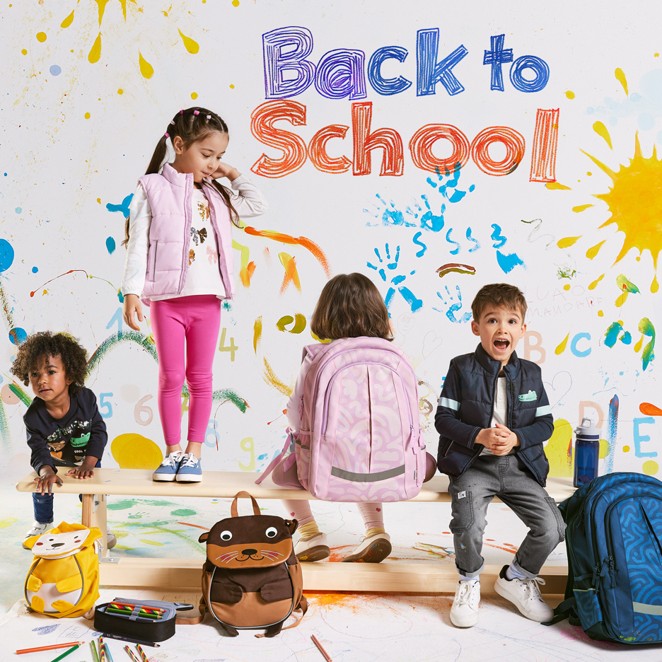 Štyri deti s batohmi a školskými potrebami, s textom „Back to School“ na farebnom pozadí.