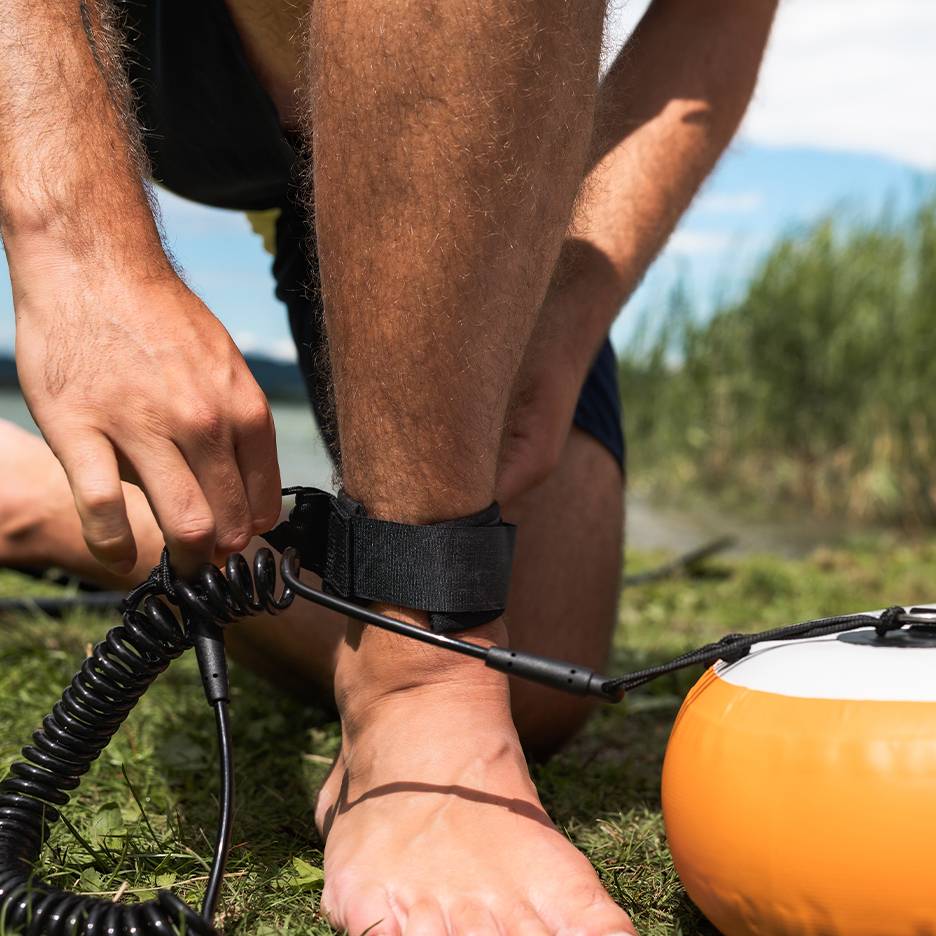Muž si pripína vodítko na paddleboard k členku.