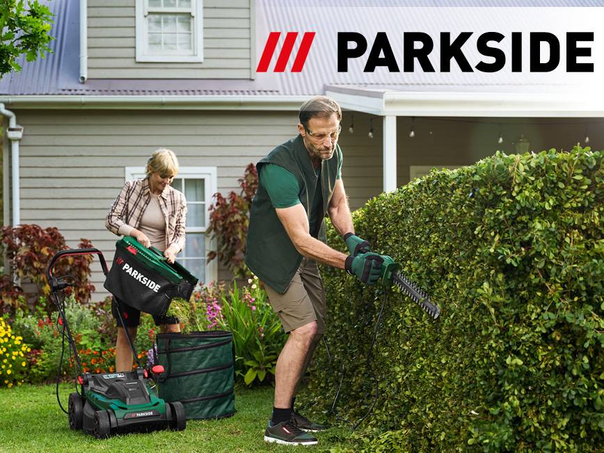 Muž strihá živý plot, zatiaľ čo žena vyprázdňuje kosačku na trávu do záhradného vaku.