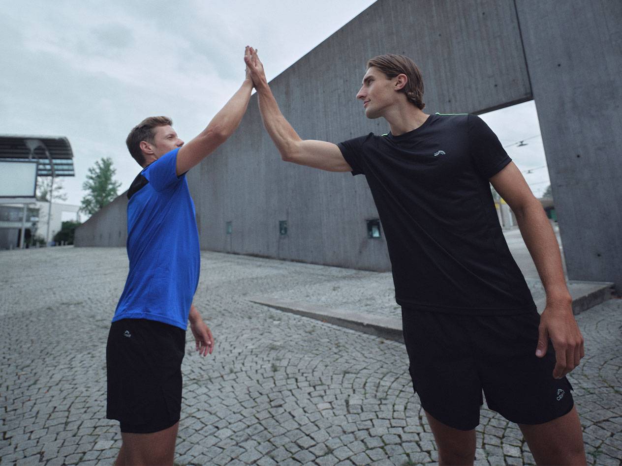 Dvaja muži v čiernych a modrých športových tričkách a šortkách si dávajú high-five.