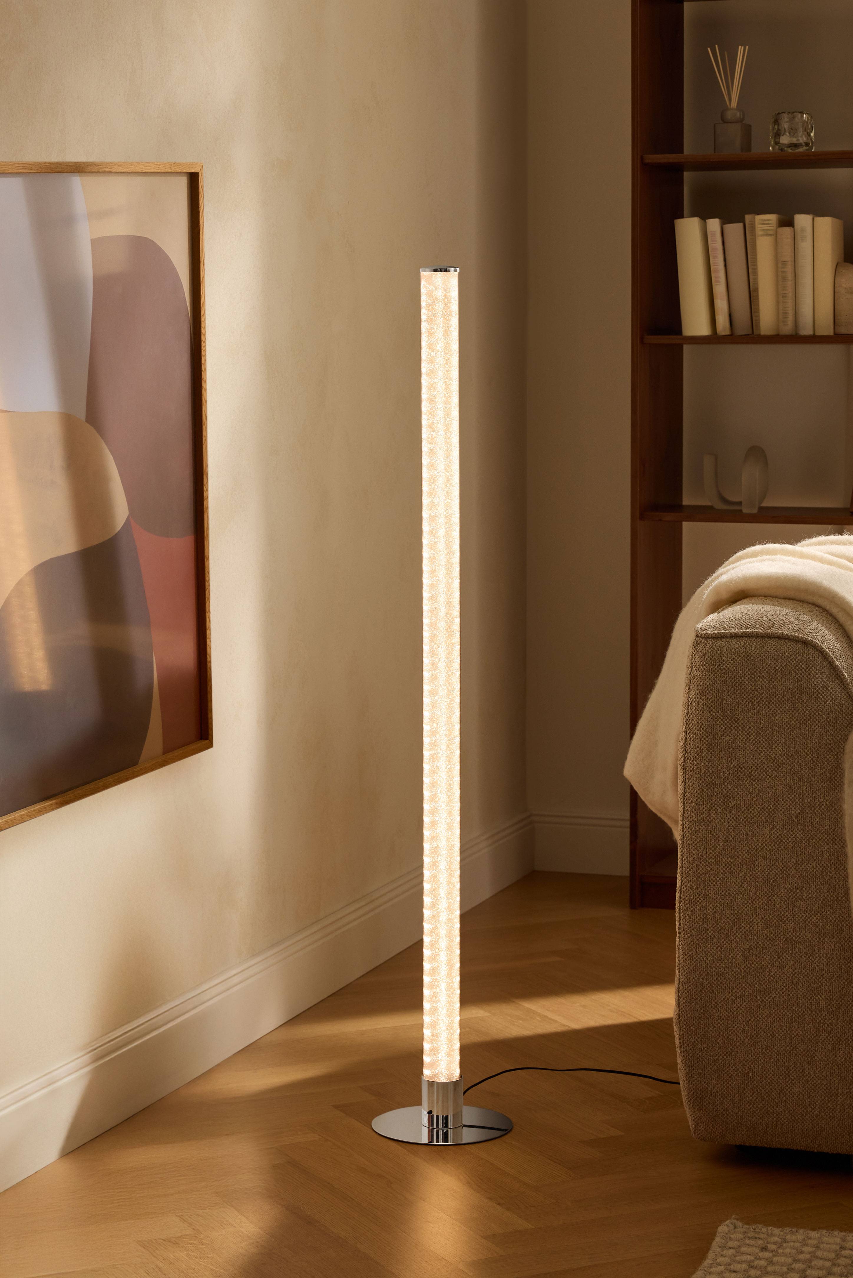 Moderná stojaca lampa v obývačke s knižnicou a pohovkou.