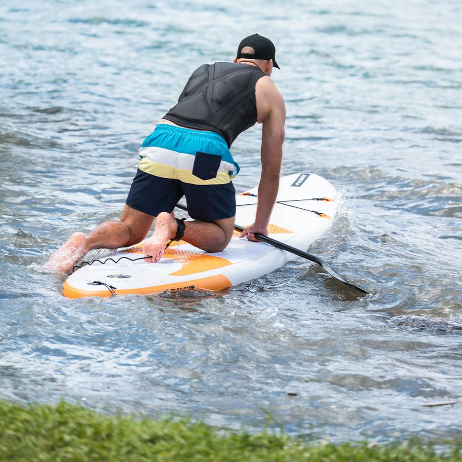 Muž kľačiaci na paddleboarde s pádlom vo vode.