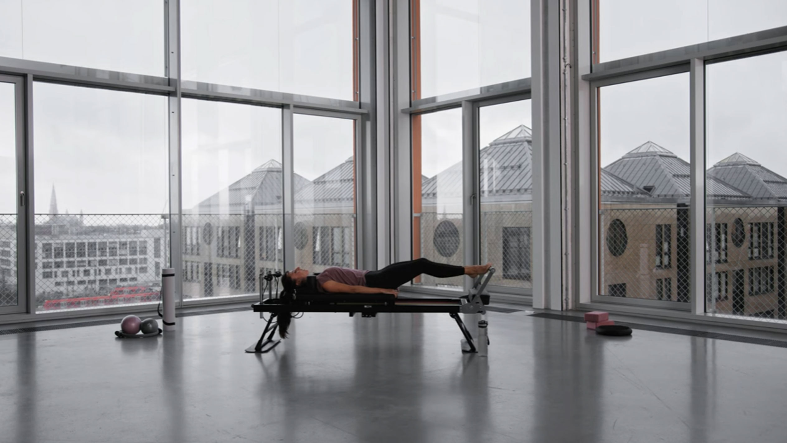 Žena cvičiaca pilates v modernom štúdiu s výhľadom na mesto.