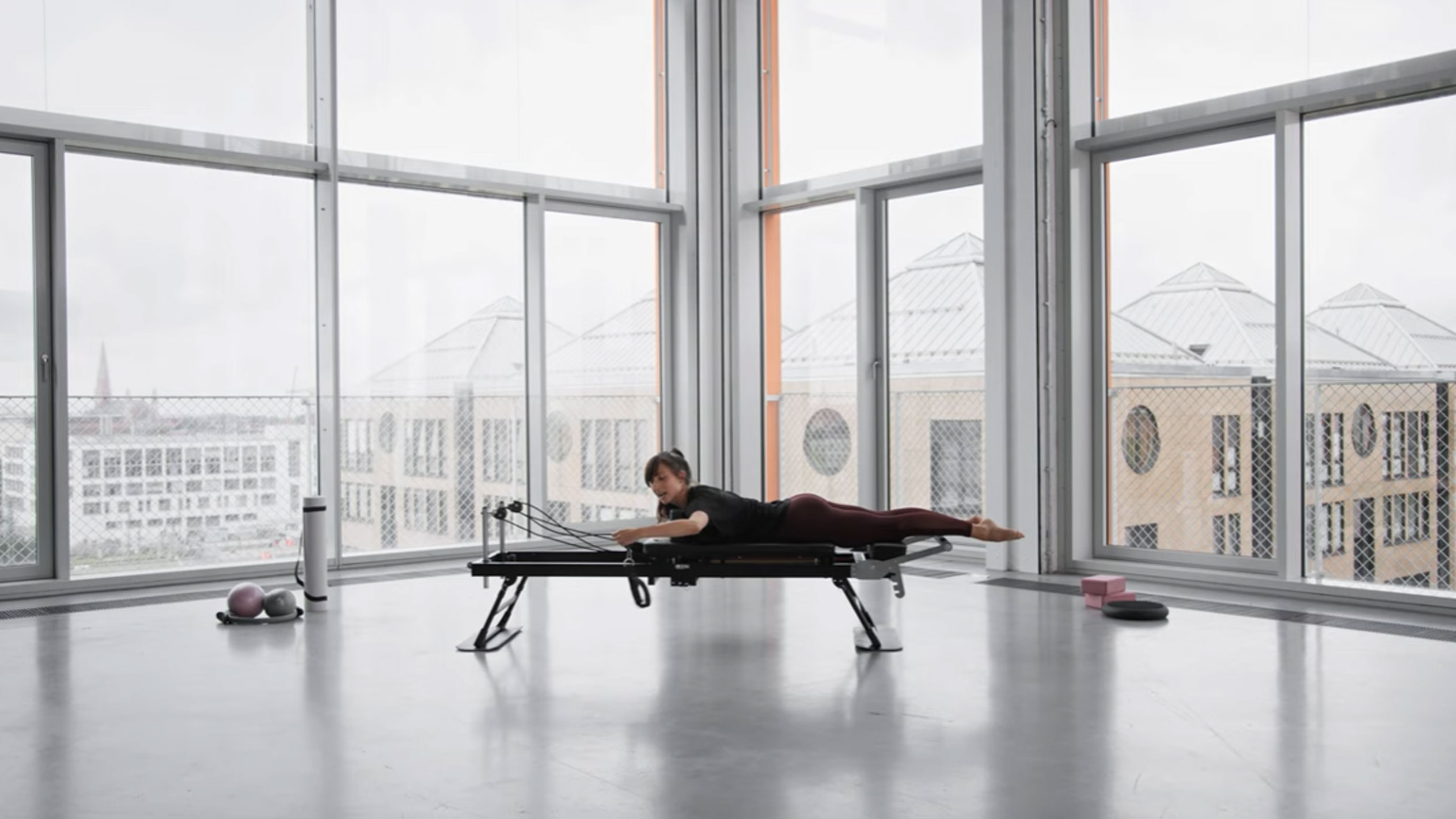 Žena cvičiaca Pilates na reformeri s výhľadom na mesto.