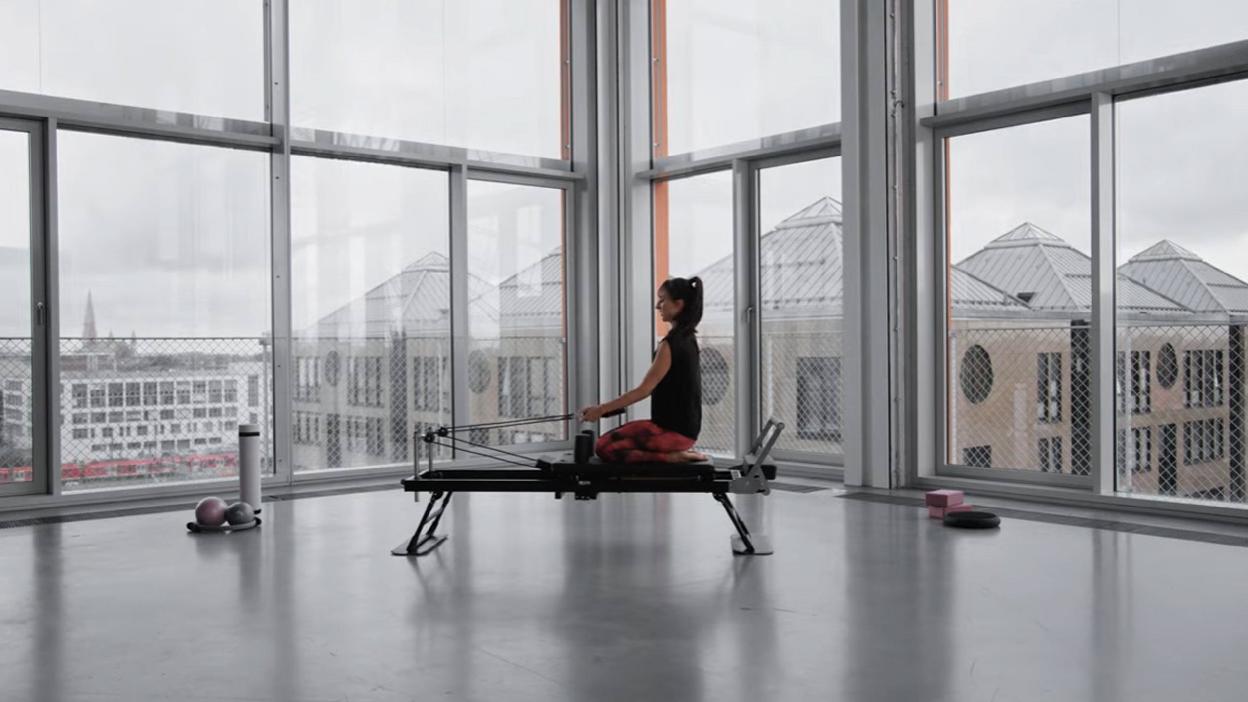 Žena cvičiaca Pilates na reformeri s výhľadom na mesto.