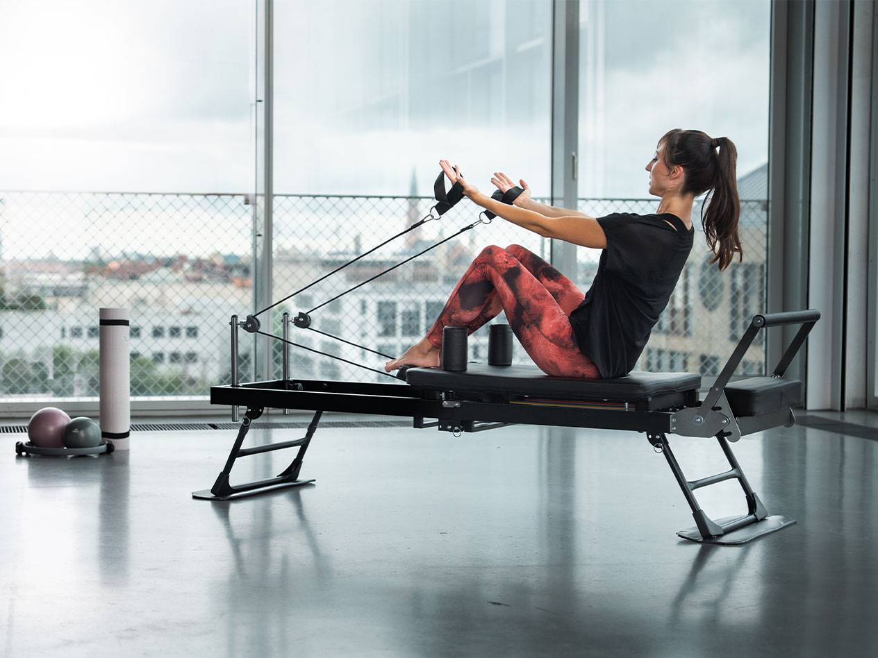 Žena cvičí pilates na reformer stroji s výhľadom na mesto.