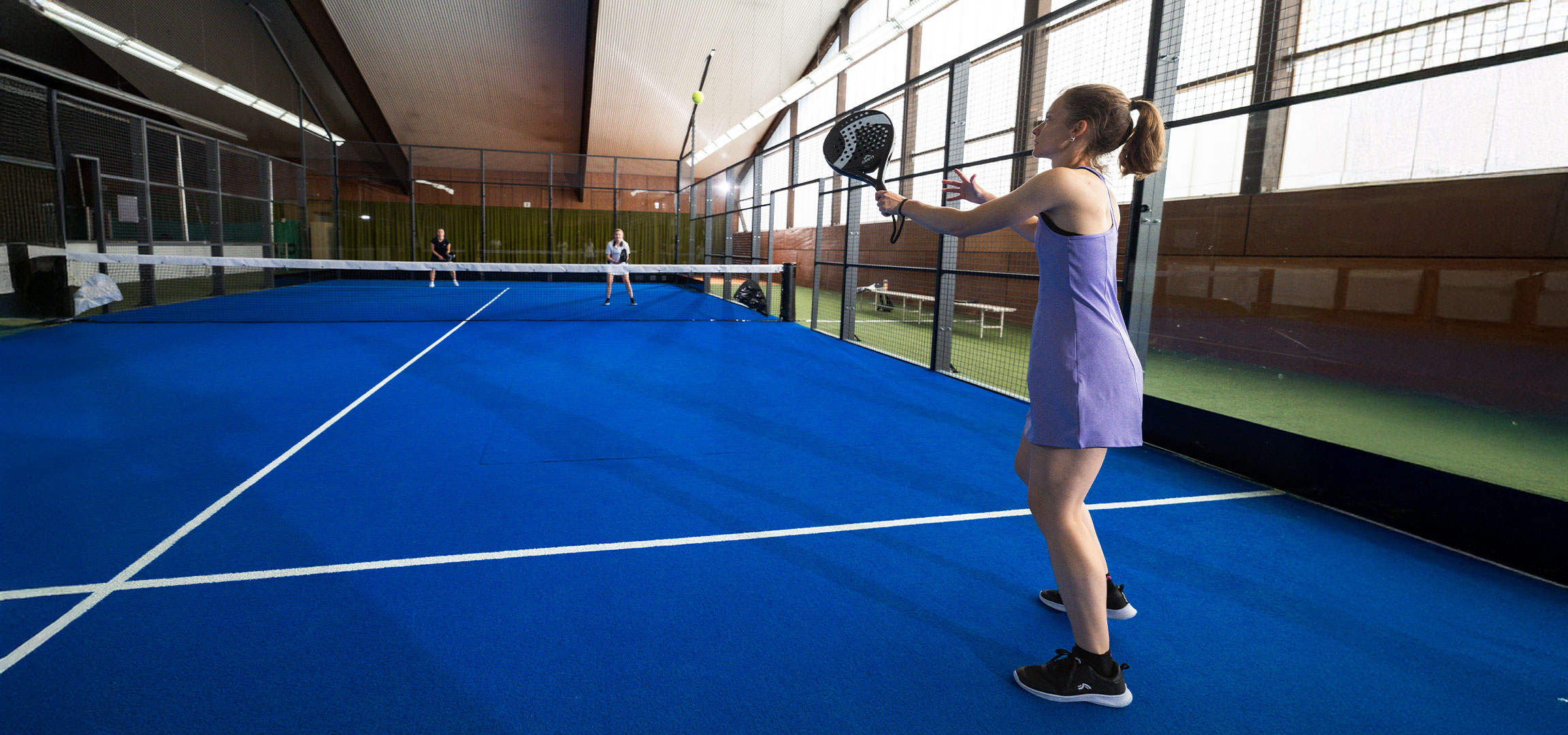 Lana Büttner hrá na kurte padel s raketou Crivit, žltou loptičkou a ďalšími hráčmi.