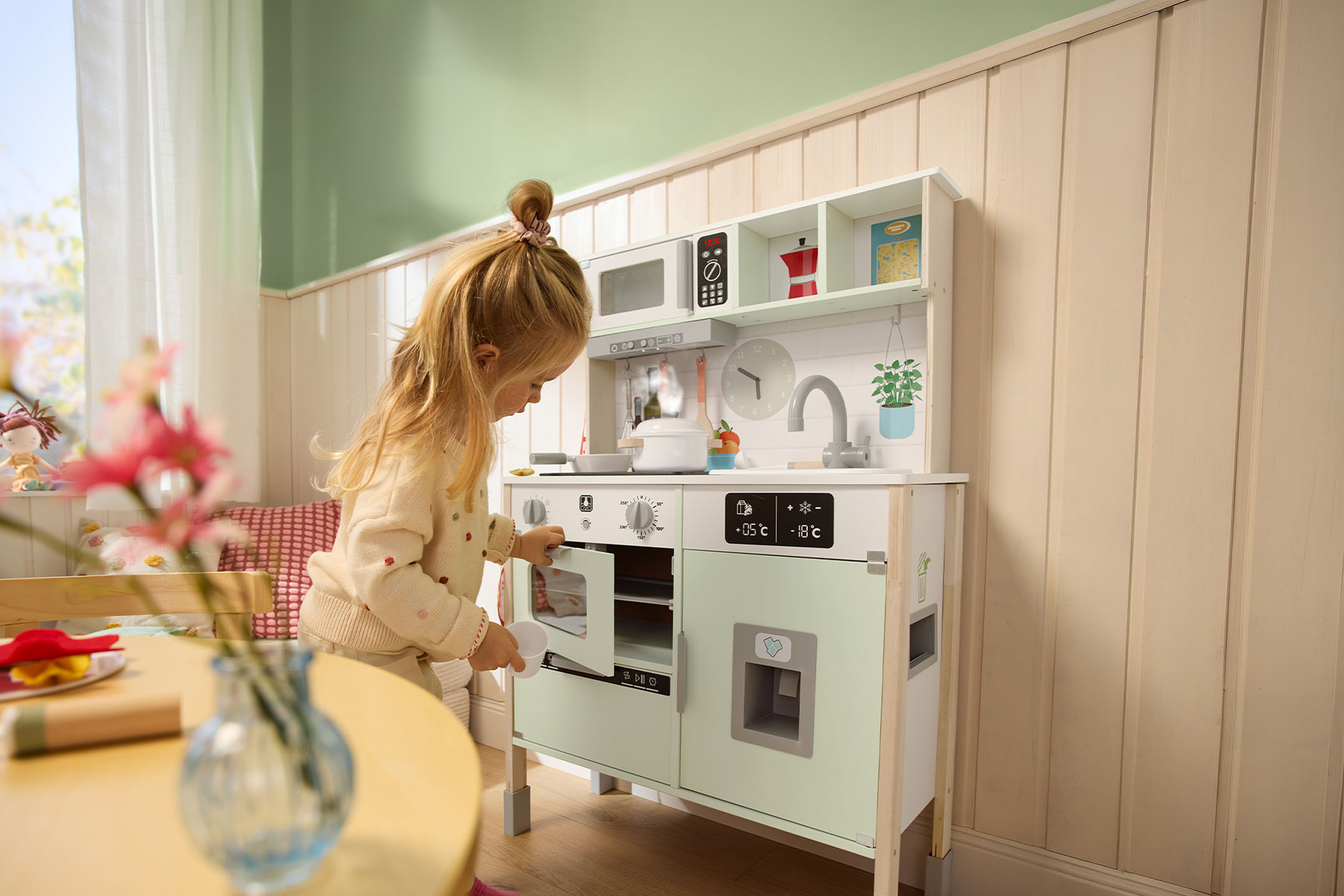 Dievčatko sa hrá s drevenou hračkárskou kuchynkou, otvára dvierka rúry.