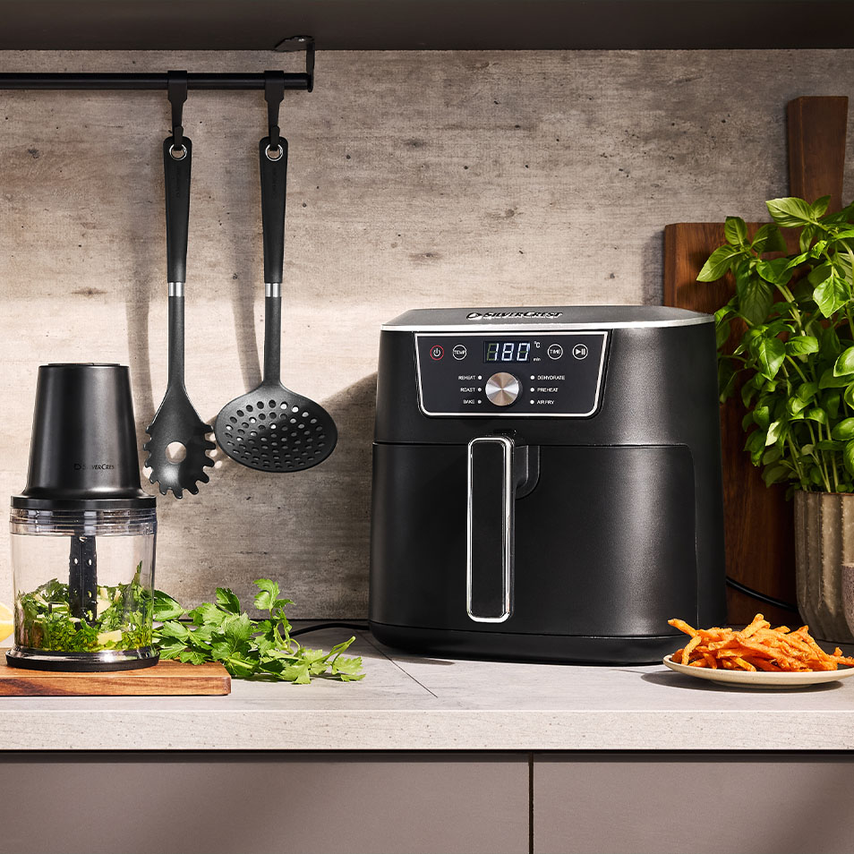 Teplovzdušná fritéza a sekáčik SilverCrest na kuchynskej linke s čerstvými bylinkami a hranolkami zo sladkých zemiakov.