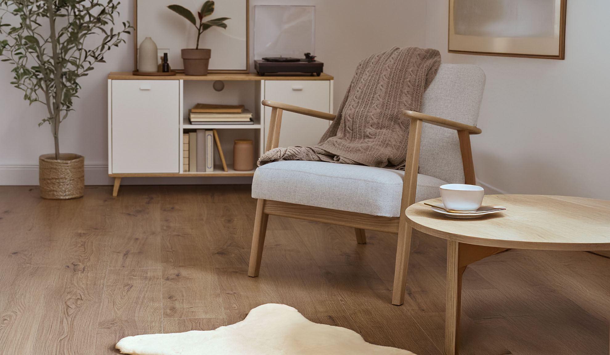 Pohodlné kreslo s dekou, drevený konferenčný stolík a úložná skrinka v svetlej obývačke.