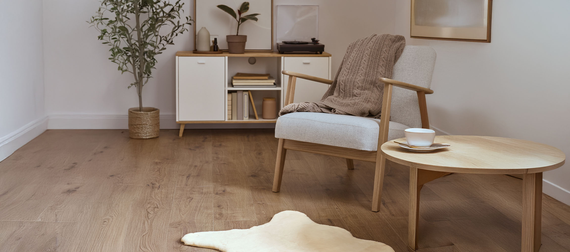 Sivé látkové kreslo s pletenou dekou, drevený konferenčný stolík a moderná komoda.