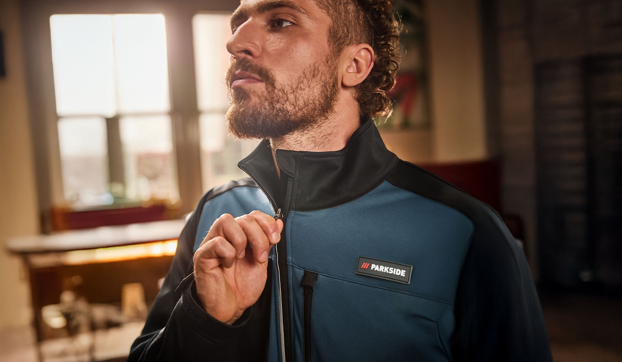 Muž v modro-čiernej pracovnej bunde Parkside, zapínajúci si ju.