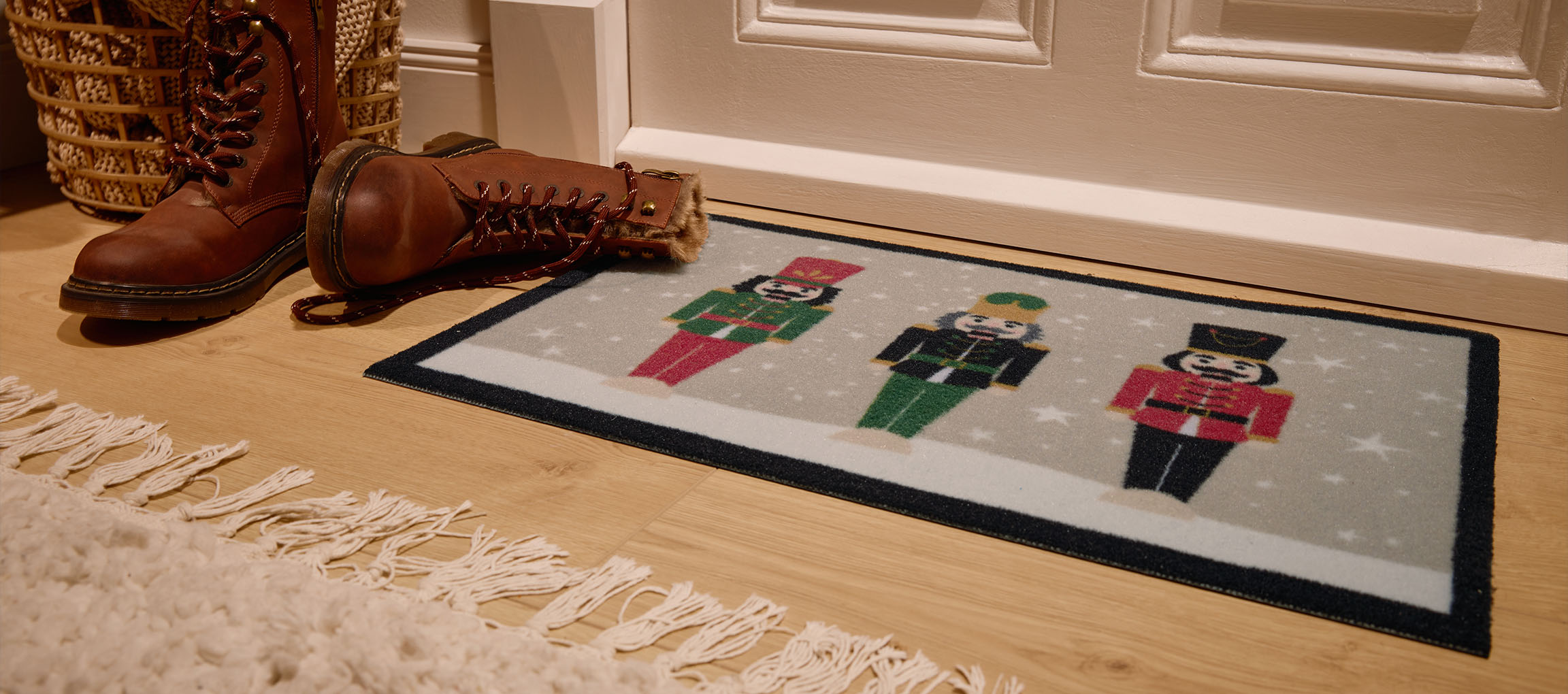 Vianočná rohožka s luskáčikmi, hnedé čižmy a prútený kôš pri vchode.