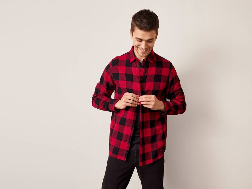 Muž zapína červeno-čiernu kockovanú košeľu.