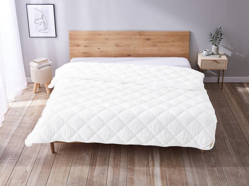 Biela prešívaná perina na posteli.