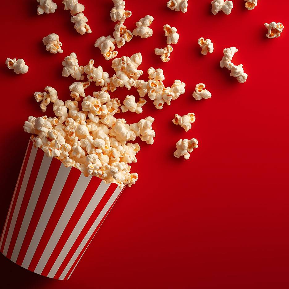 Popcorn na červenom pozadí, časť popcornu v pruhovanom kartónovom pohári.