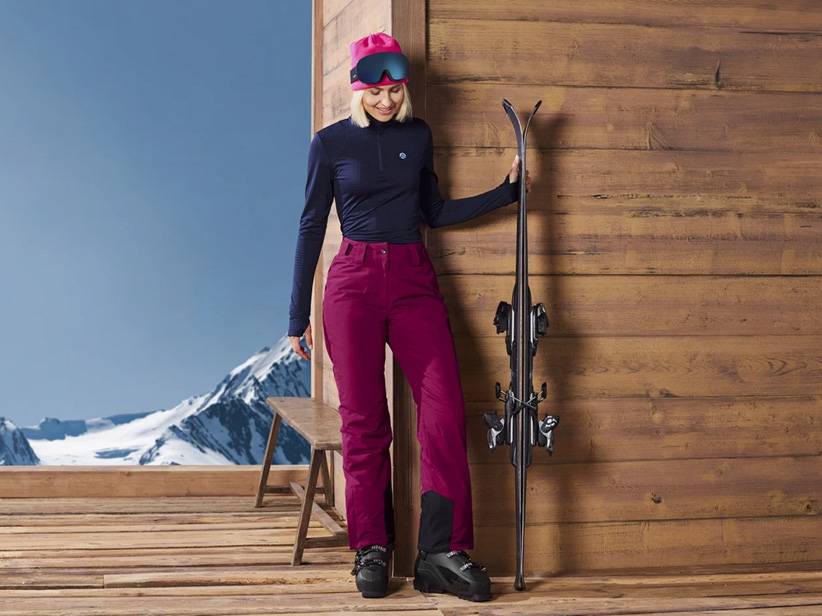 Dámske lyžiarske oblečenie: bordové nohavice, čierny top a lyže.