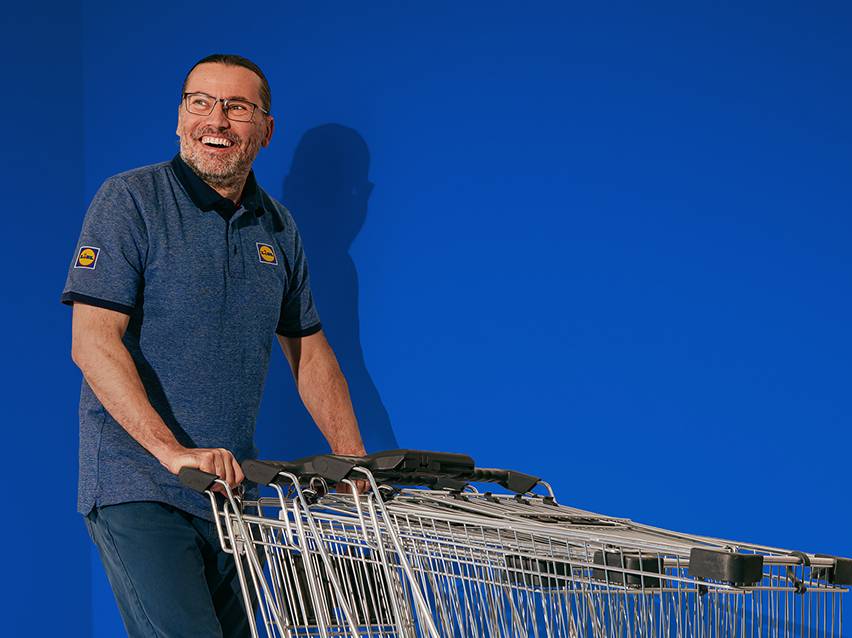 Muž v modrom tričku s nákupnými vozíkmi na modrom pozadí.