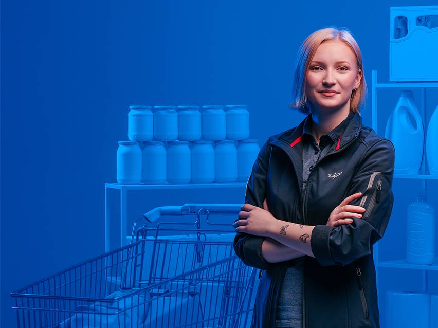 Mladá žena v obchode s potravinami, v pozadí sú poháre a nákupný vozík.